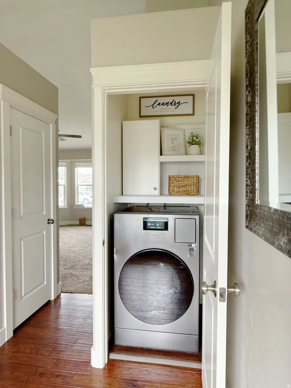 Dedicated laundry closet featuring a stainless steel front-load appliance, built-in shelving, and upper cabinetry