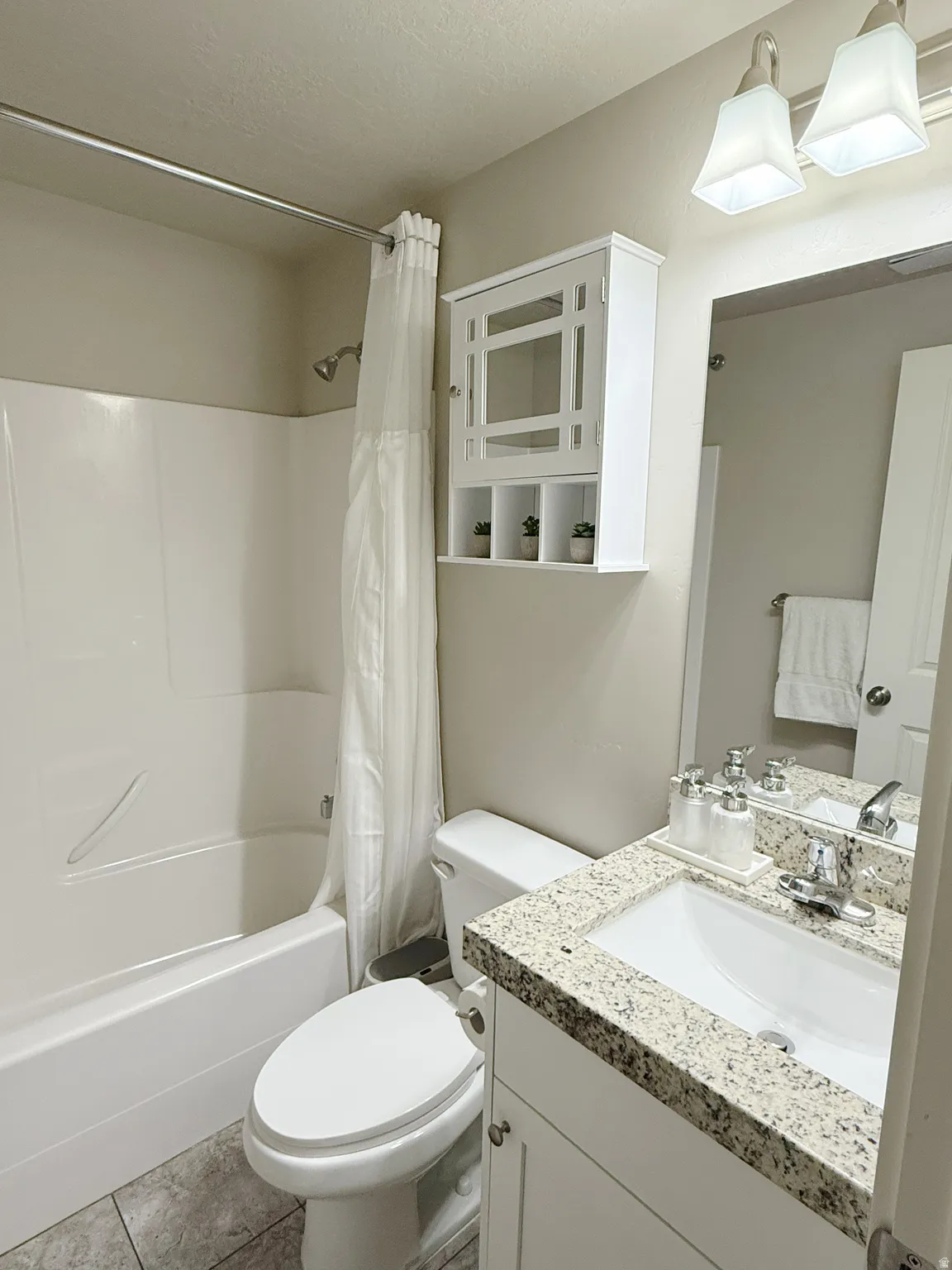 Bathroom featuring a white bathtub/shower combination, a white toilet, and a vanity with a granite-finish countertop