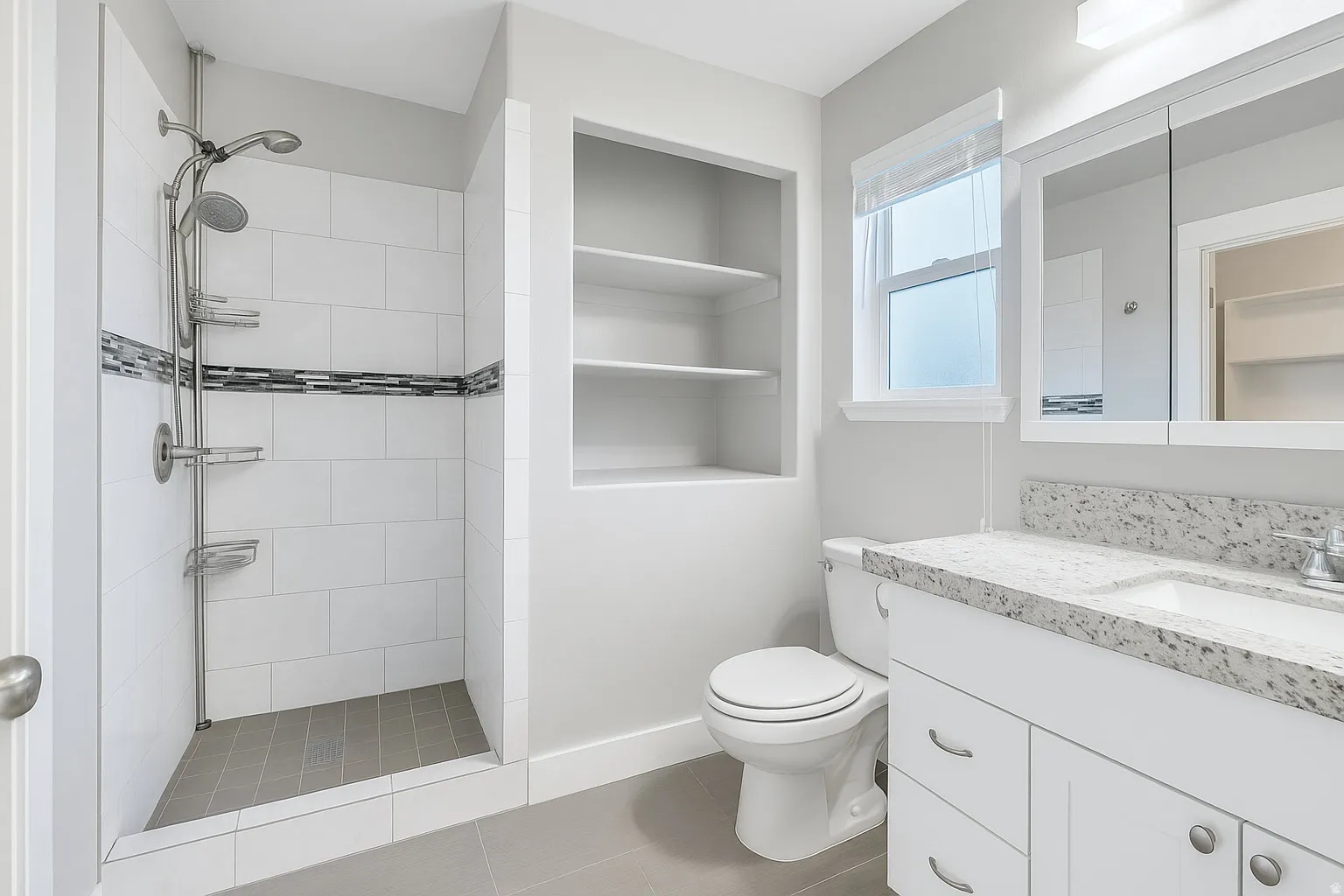 Bathroom featuring a walk-in shower with tile surround and decorative accent band, a built-in wall niche with shelving, a vanity with a light-toned countertop, and a mirrored medicine cabinet