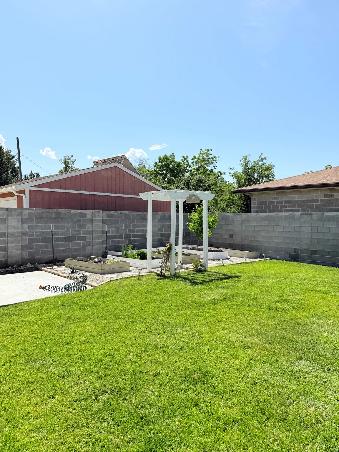 Expansive grassy lawn with a concrete patio area, perimeter block wall, and white pergola