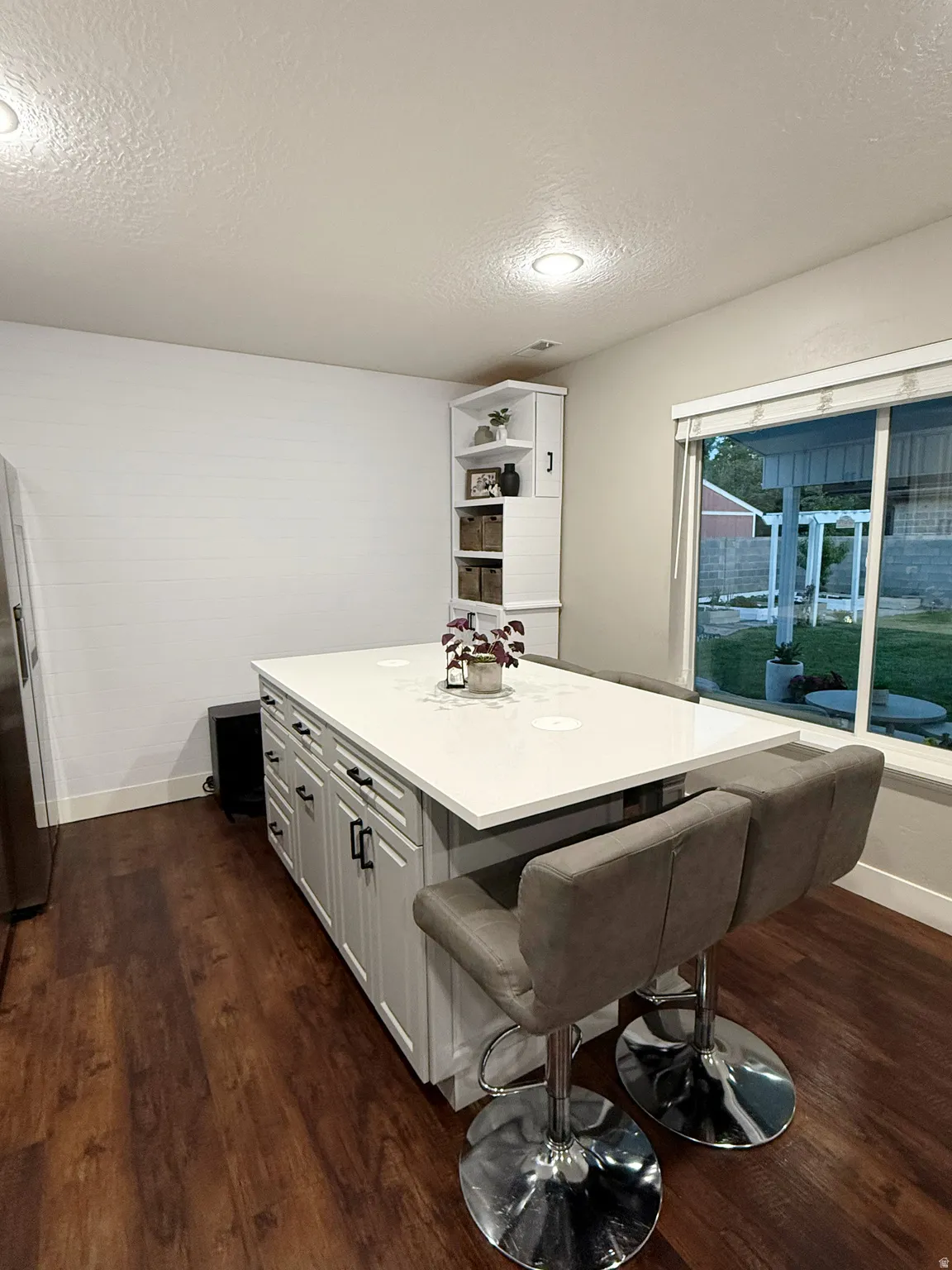 Kitchen island featuring a light-colored countertop with integrated outlets, white cabinetry with black hardware, and wood-finish flooring