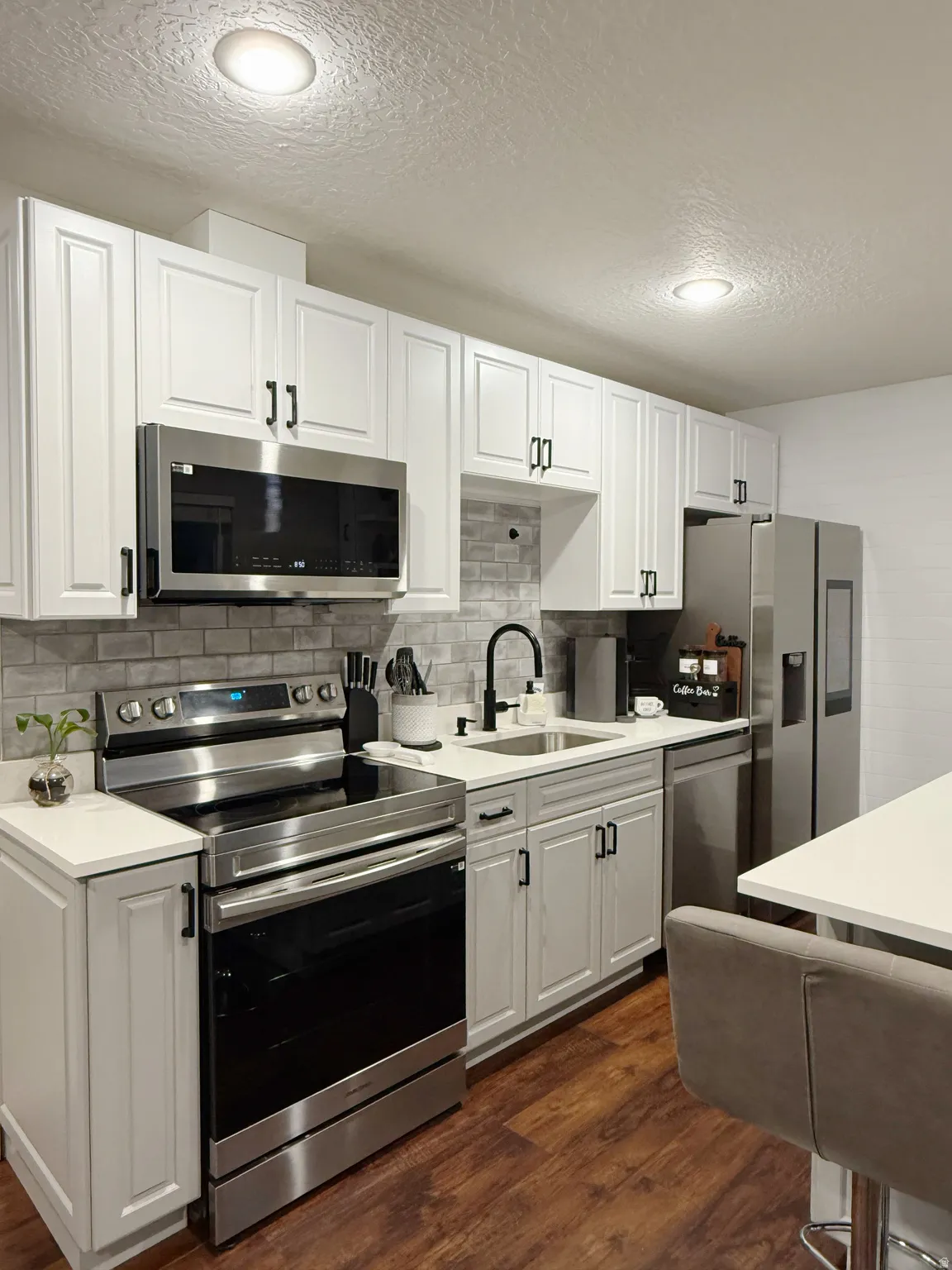 Modern kitchen featuring white shaker cabinetry with dark hardware, stainless steel appliances, a subway tile backsplash, and wood-finish flooring
