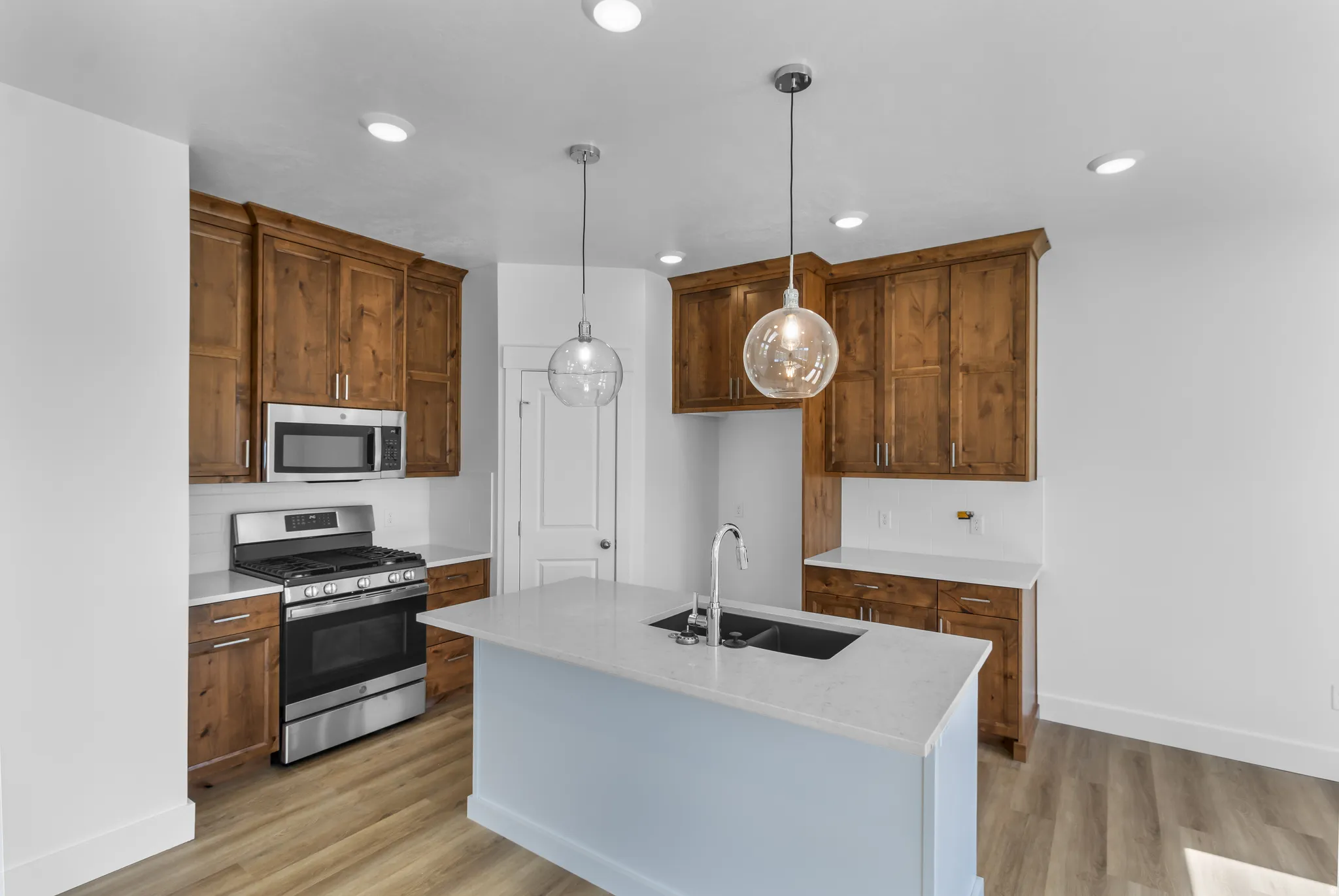 Kitchen featuring a central island with a dual-basin sink, pendant lighting, stainless steel appliances, wood-finish cabinetry, and light-toned countertops