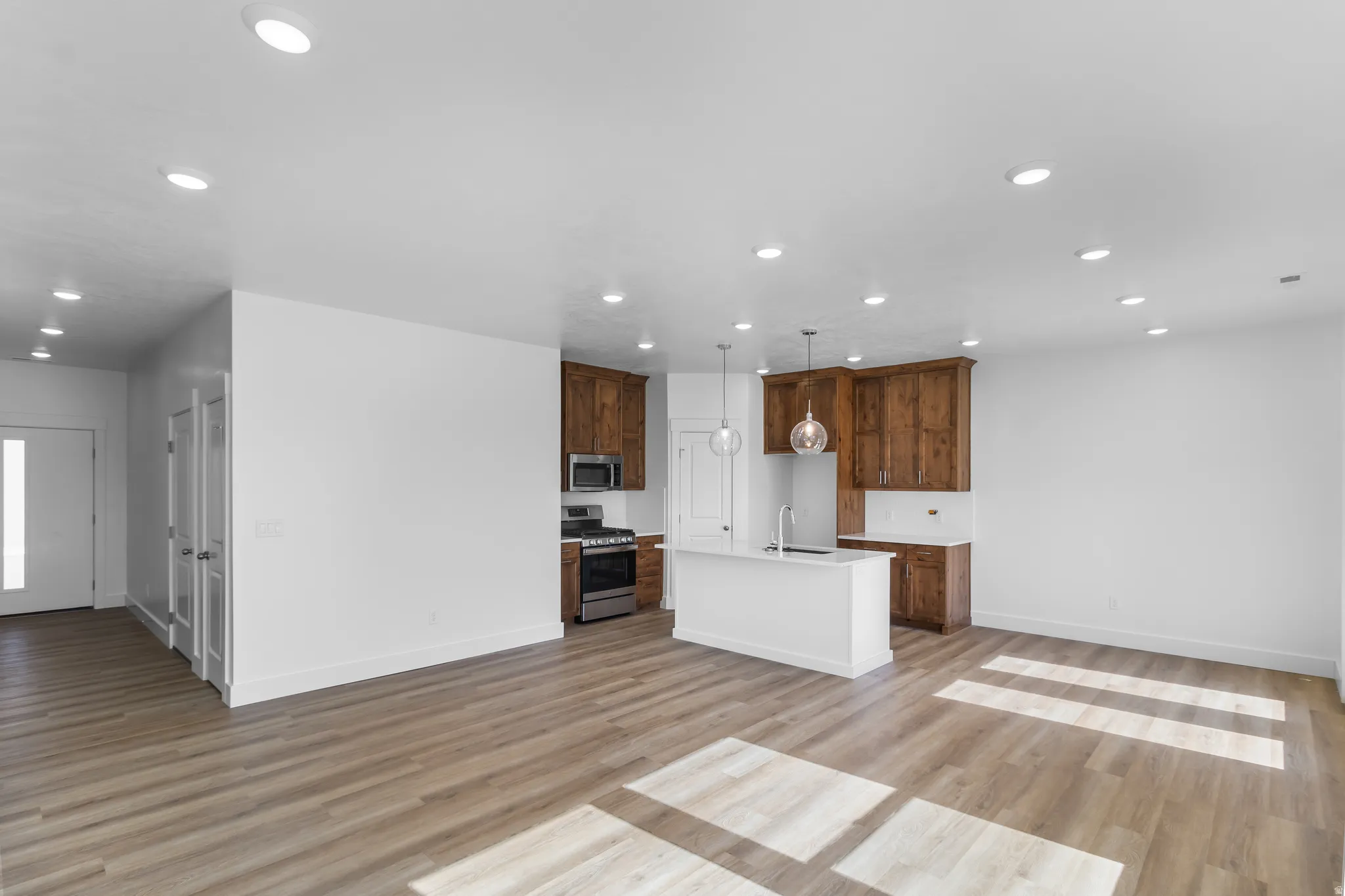 Open-concept living space featuring wood-finish flooring, recessed lighting, and a kitchen with warm-toned cabinetry, a white island, and stainless steel appliances