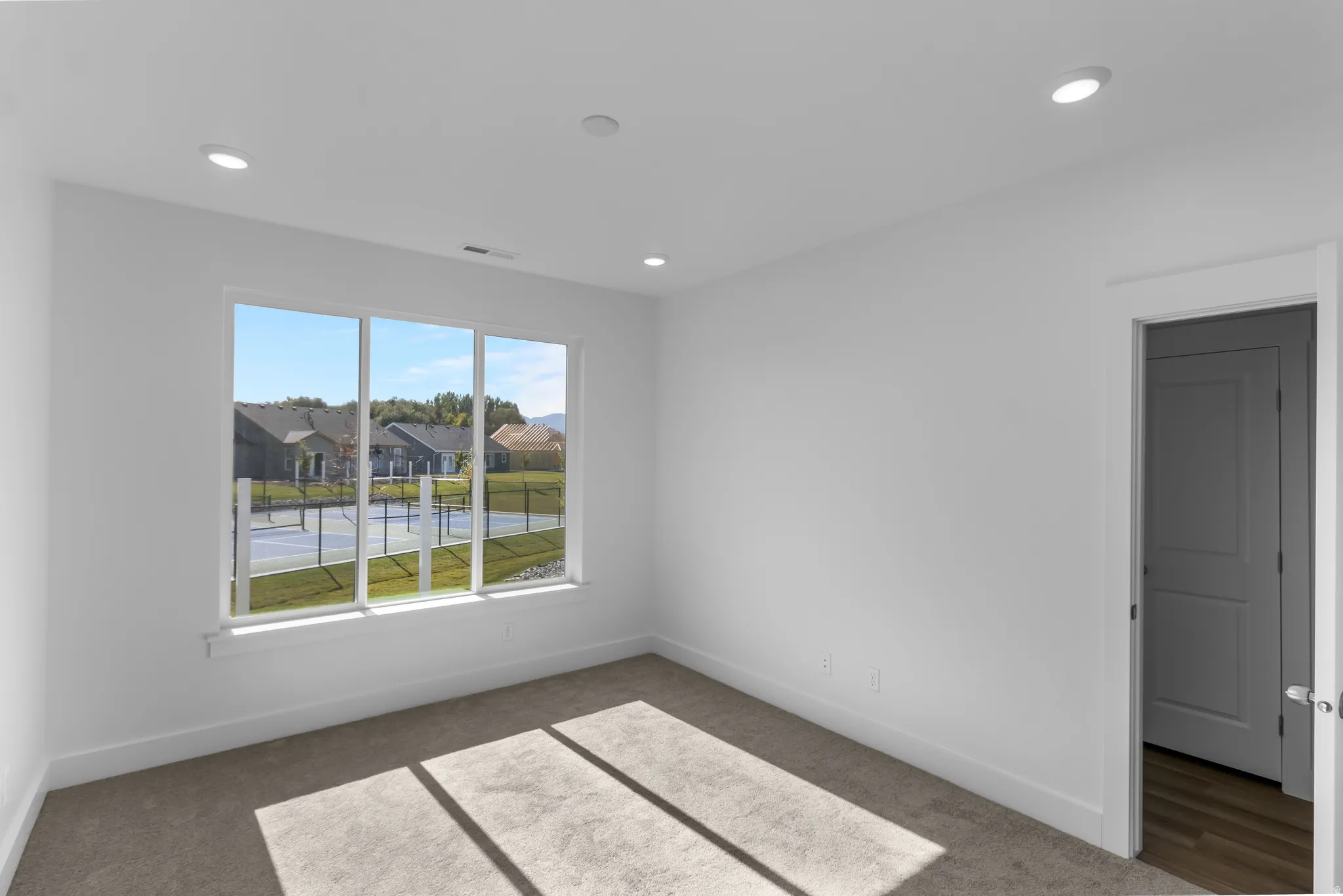 Room featuring a large triple-pane window, recessed ceiling lighting, light gray carpeting, crisp white walls, and a white baseboard trim