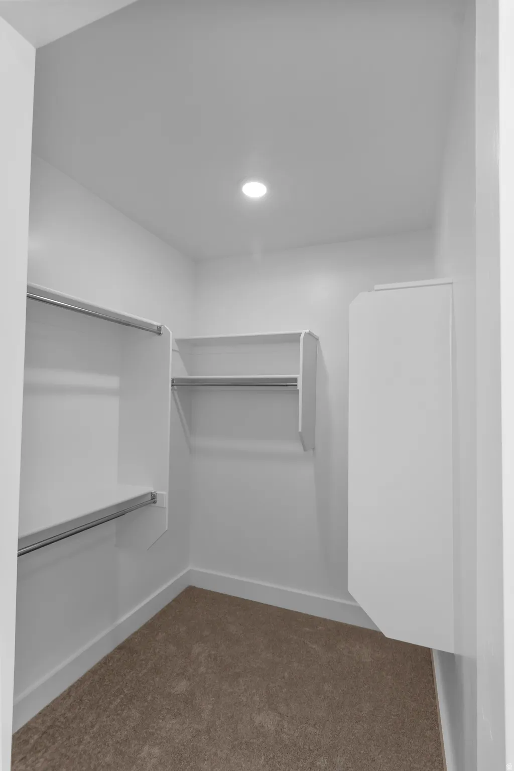 Walk-in closet featuring built-in shelving, hanging rods, recessed ceiling lighting, light-toned carpeting, and white baseboards