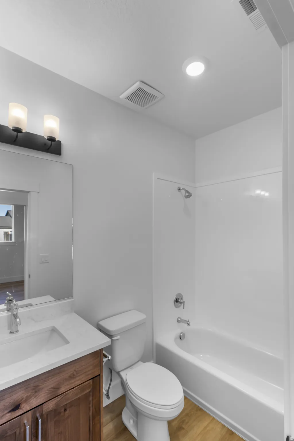 Bathroom featuring a wood-finish vanity with a single basin sink and stone-look countertop, a white toilet, and a white tub/shower combination with chrome fixtures