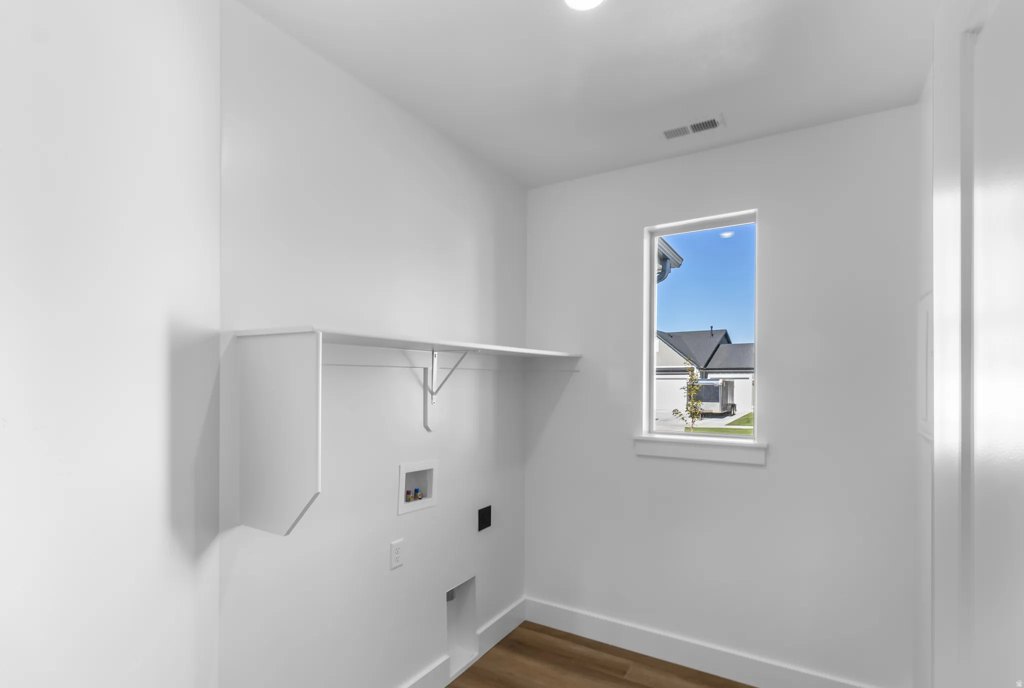 Dedicated laundry area featuring white walls, wood-finish flooring, a built-in shelf, and a window with white trim