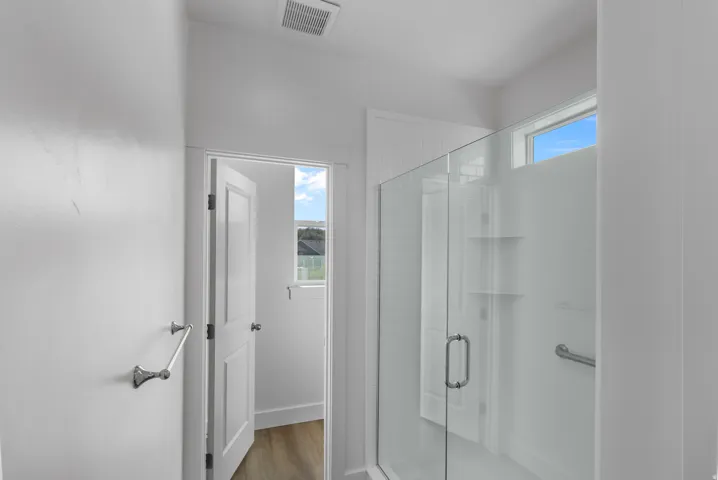 Glass-enclosed shower with white subway tile, built-in shelving, and a chrome grab bar
