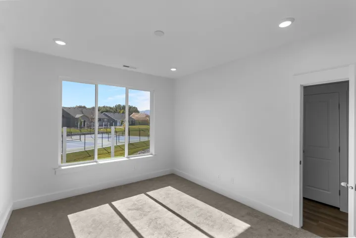 Room featuring a large triple-pane window, recessed ceiling lighting, light gray carpeting, crisp white walls, and a white baseboard trim