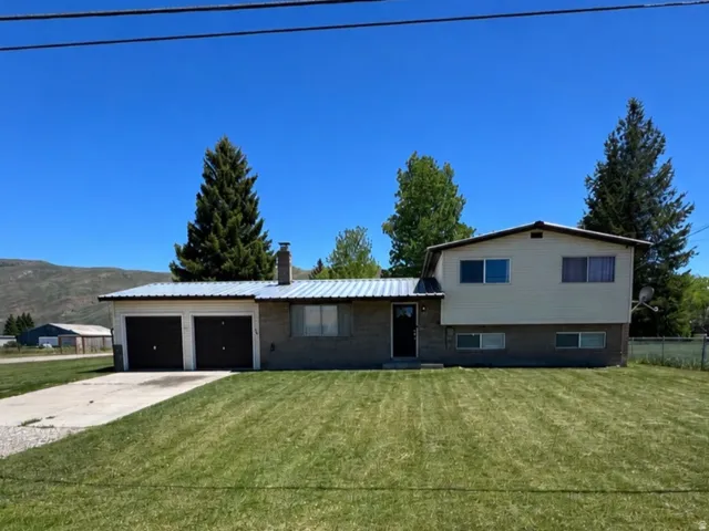 Split-level residence featuring a two-car garage with dark garage doors, a concrete driveway, and a spacious front lawn
