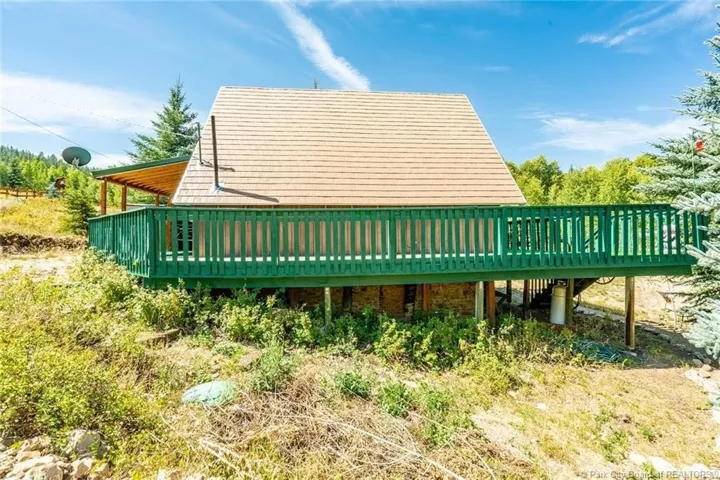 Elevated outdoor deck with green railing and slatted privacy screen, featuring a covered patio extension with wood ceiling and exposed beams