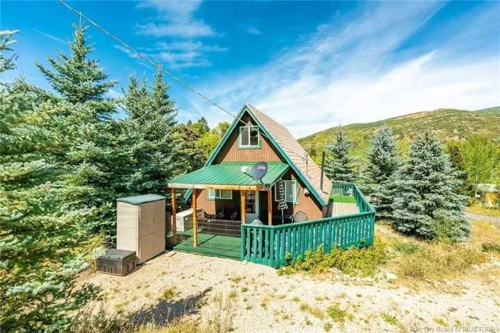 A-frame cabin featuring a green metal roof, a covered porch, and an exterior deck with green railing