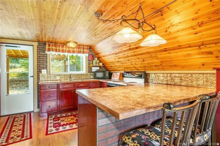 Kitchen featuring wood-finish flooring, wood plank ceiling, red cabinetry, brick accents, and a built-in kitchen island with stone-look countertop