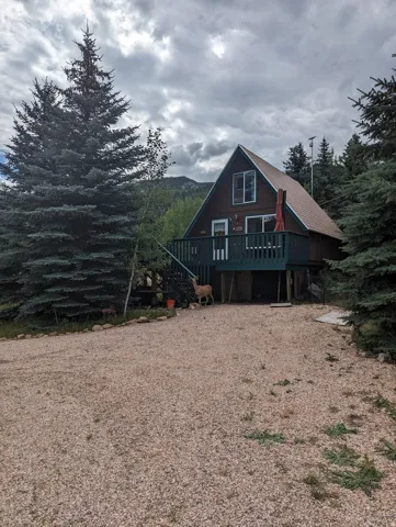 A-frame dwelling with a brown exterior and a dark green deck, featuring a gabled roof and multiple windows