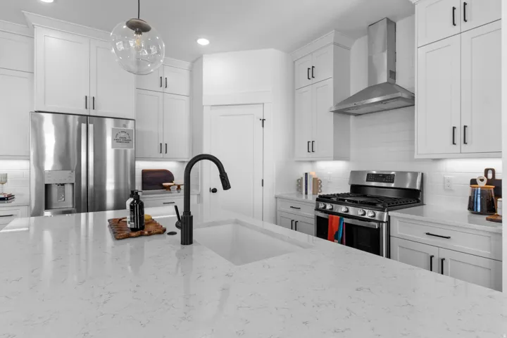 Bright kitchen featuring a large island with an integrated sink and matte black faucet, stainless steel appliances, white cabinetry, and recessed lighting