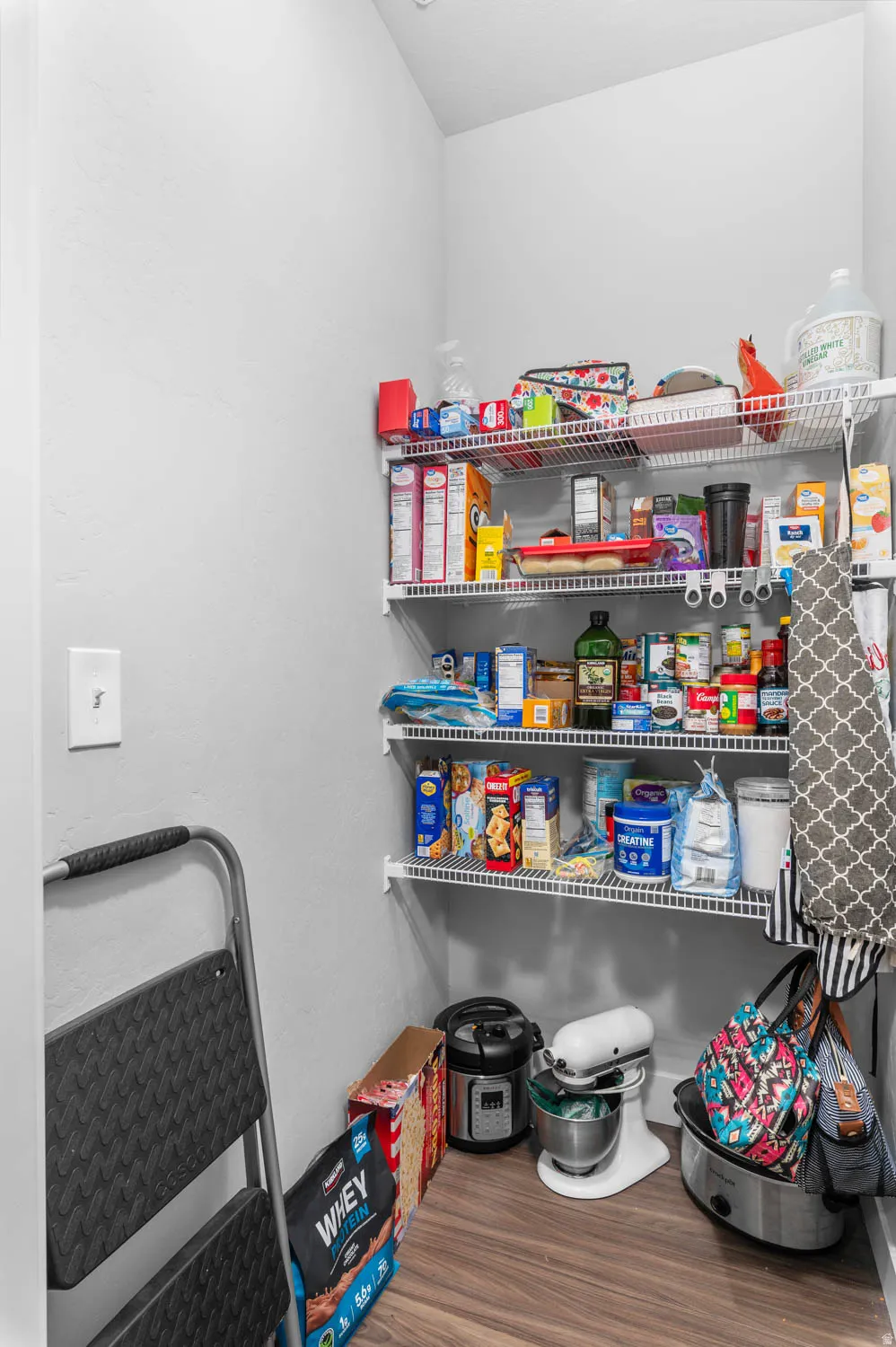 Spacious pantry featuring multiple wire shelving units, light-toned walls, and wood-finish flooring