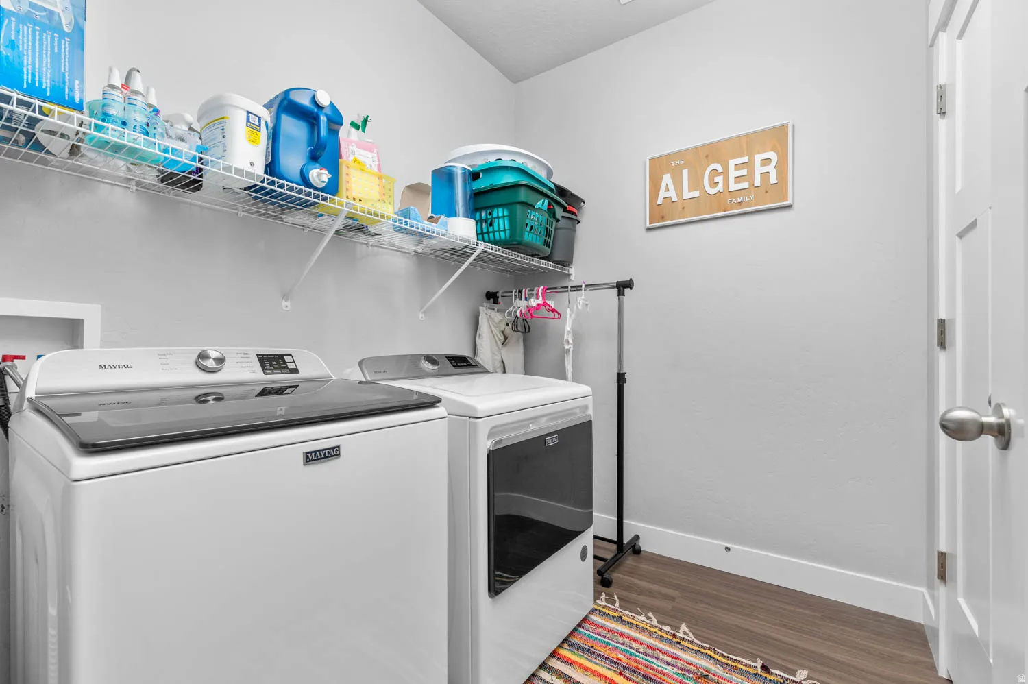 Dedicated laundry area featuring white walls, durable wood-finish flooring, and two integrated wire shelving units for storage