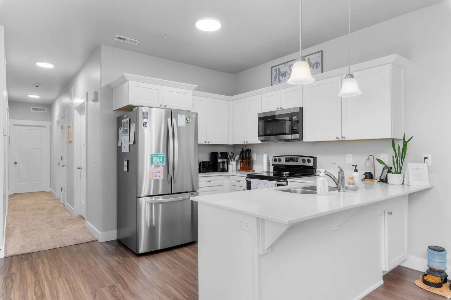 Modern kitchen featuring white shaker cabinetry, stainless steel appliances, and wood-finish flooring