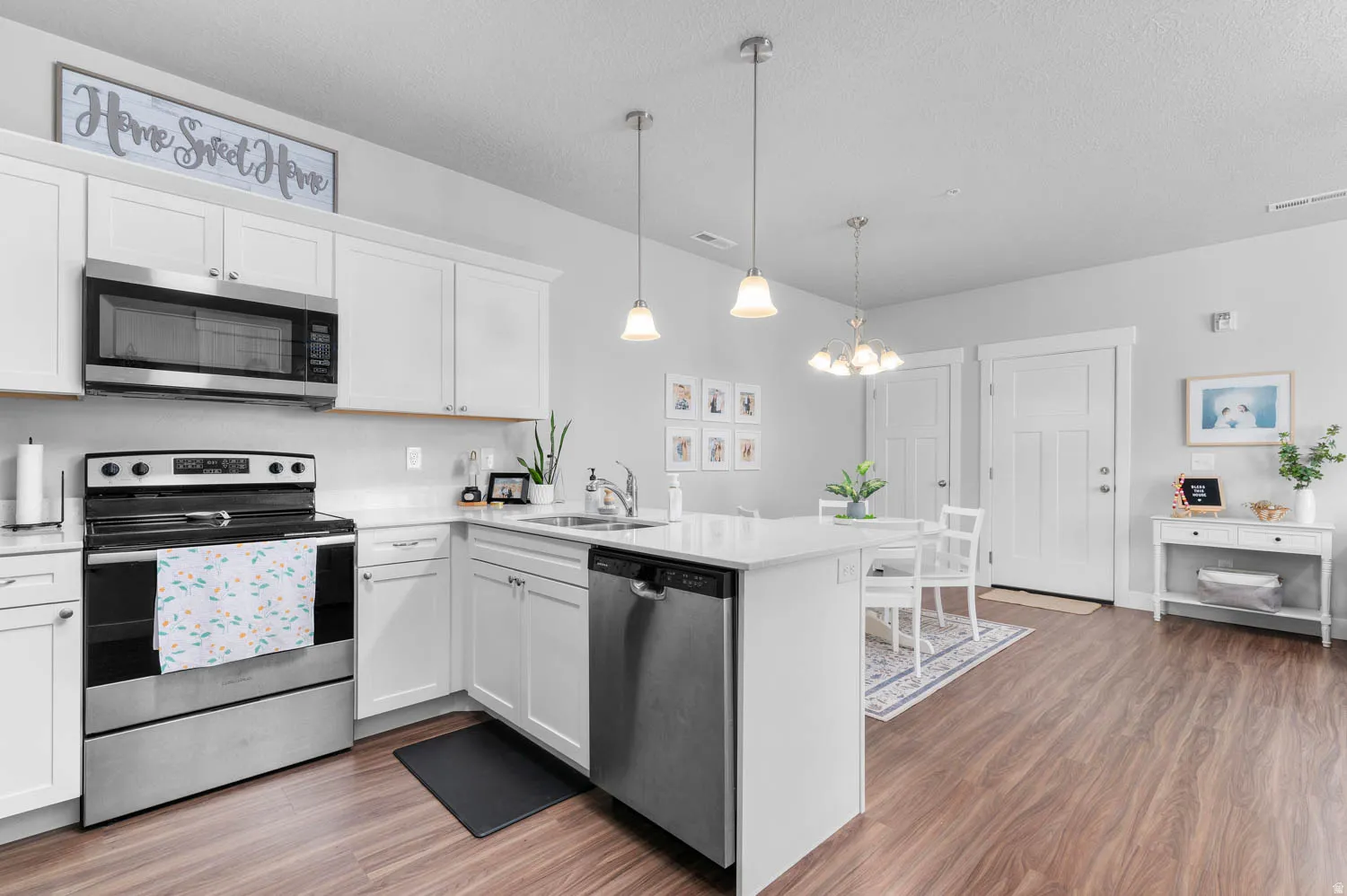 Open-concept kitchen featuring white cabinetry, stainless steel appliances, a center island with sink, pendant lighting, and wood-finish flooring