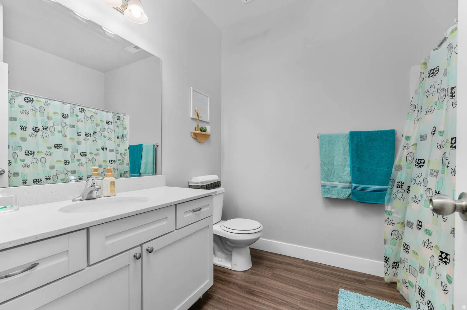 Bathroom featuring a wood-finish floor, white vanity with a light-colored countertop, and a shower with a privacy curtain