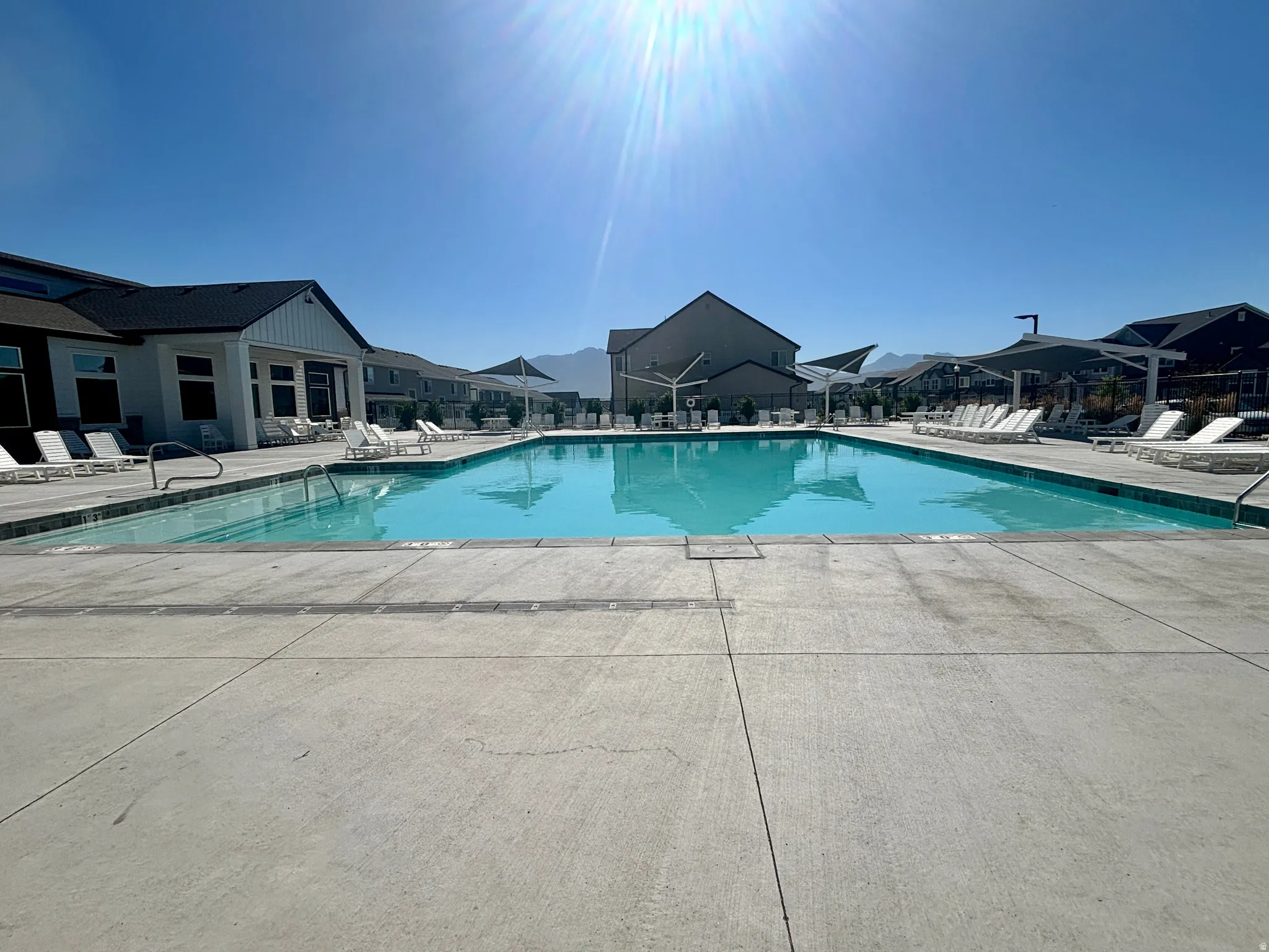 Expansive outdoor swimming pool with surrounding concrete decking, shaded lounge areas, and a clubhouse structure