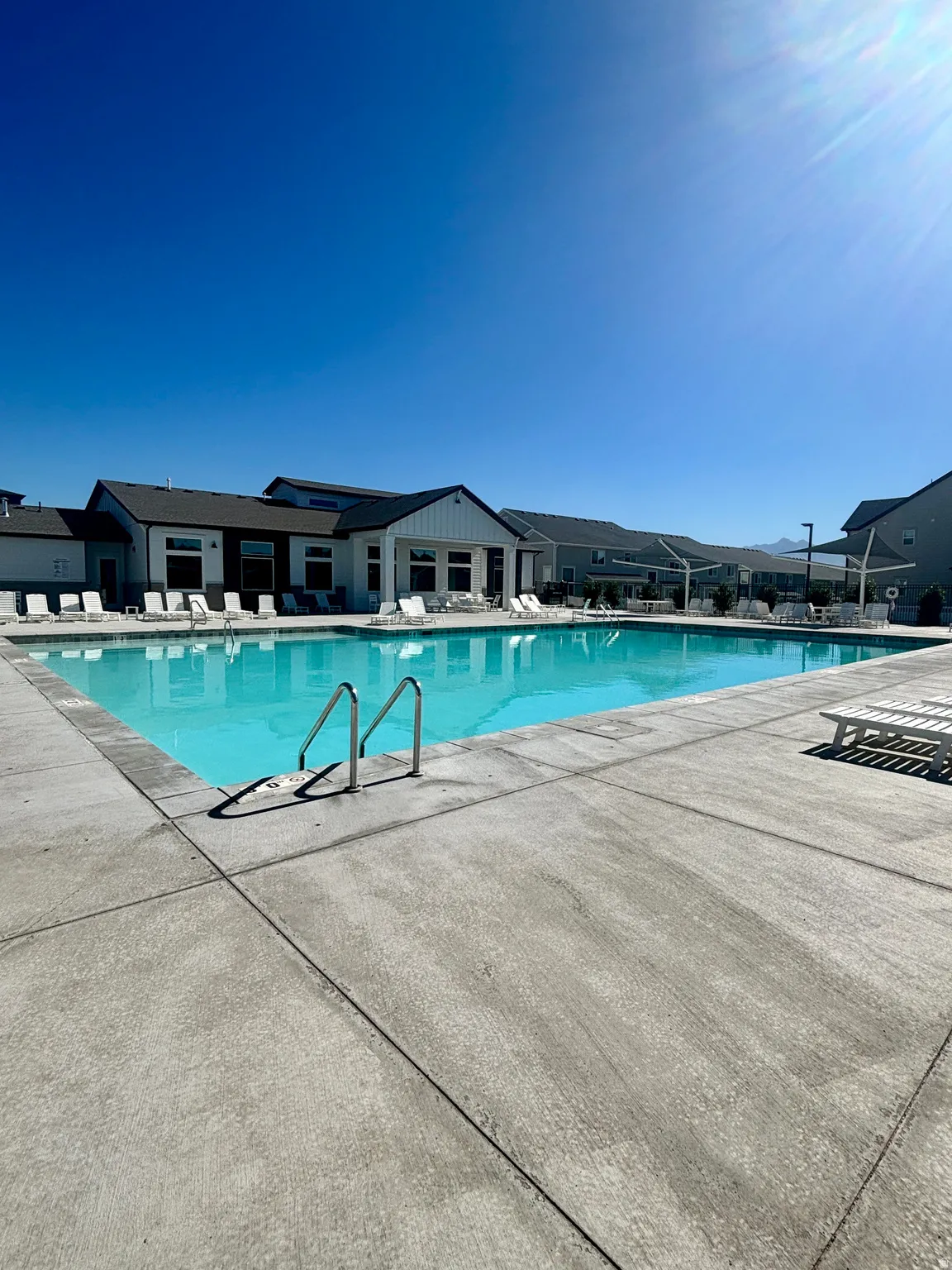 Community pool with concrete decking, surrounding structures with dark siding and white vertical paneling, and mountains visible in the distance