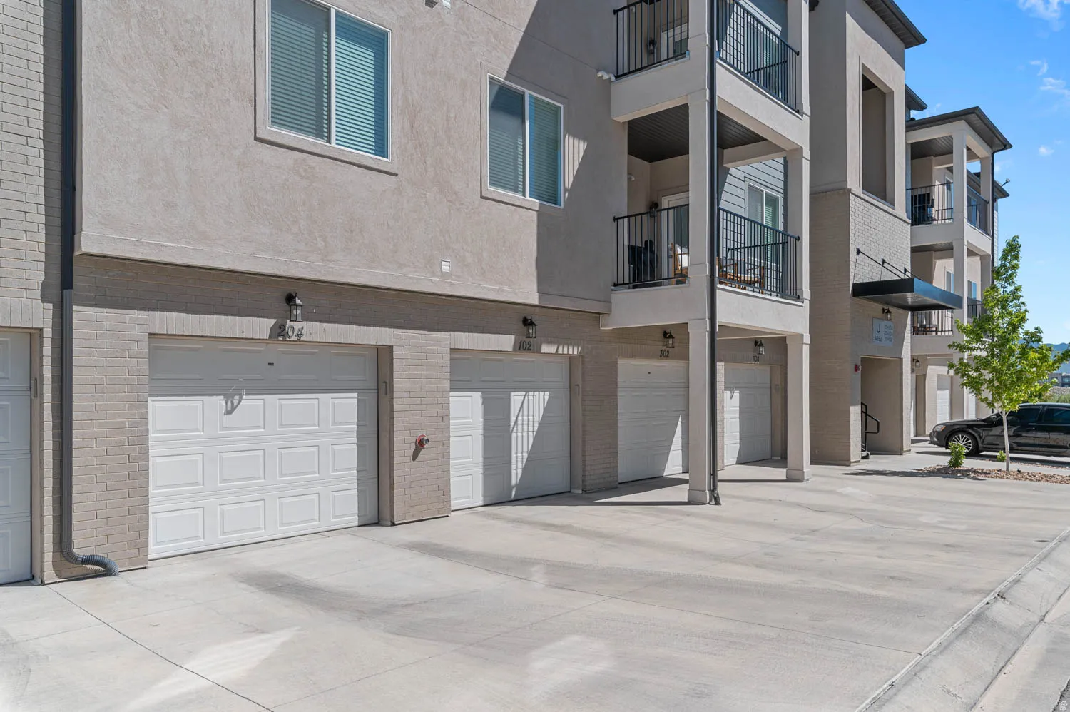 Exterior facade featuring individual garages, private balconies with black railings, and a combination of stucco and brick finishes