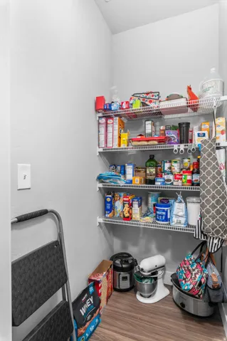 Spacious pantry featuring multiple wire shelving units, light-toned walls, and wood-finish flooring