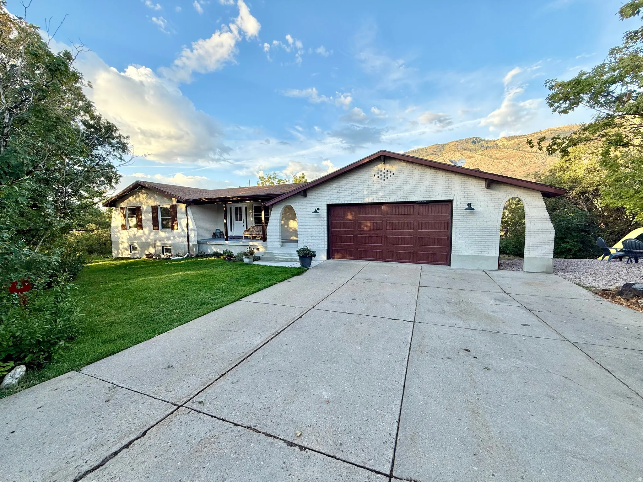 Ranch-style exterior with a split-level design, featuring a two-car garage with an arched entryway, a concrete driveway, a manicured lawn, and mature landscaping
