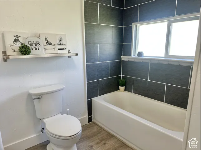 Bathtub with dark grey subway tile surround, integrated window, and wood-finish flooring
