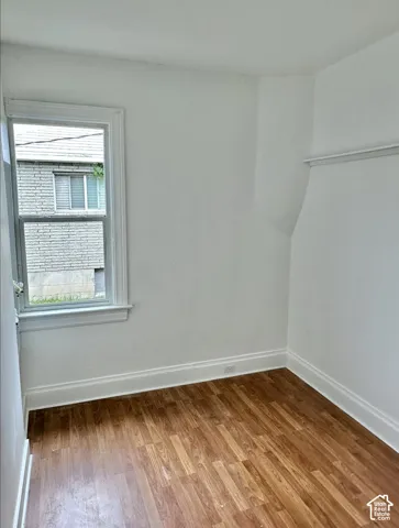 Bright room featuring wood-finish flooring, white painted walls, a single window, and white trim