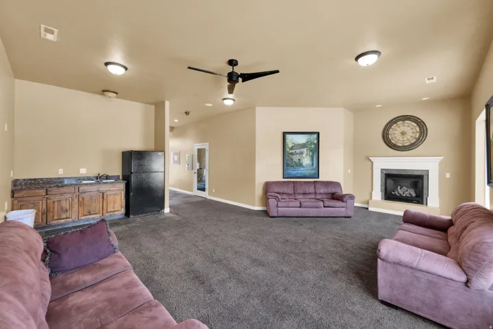 Club House-Spacious room featuring a built-in wet bar with wood cabinetry and stone-look countertop, a gas fireplace with a white mantel, and ceiling-mounted lighting