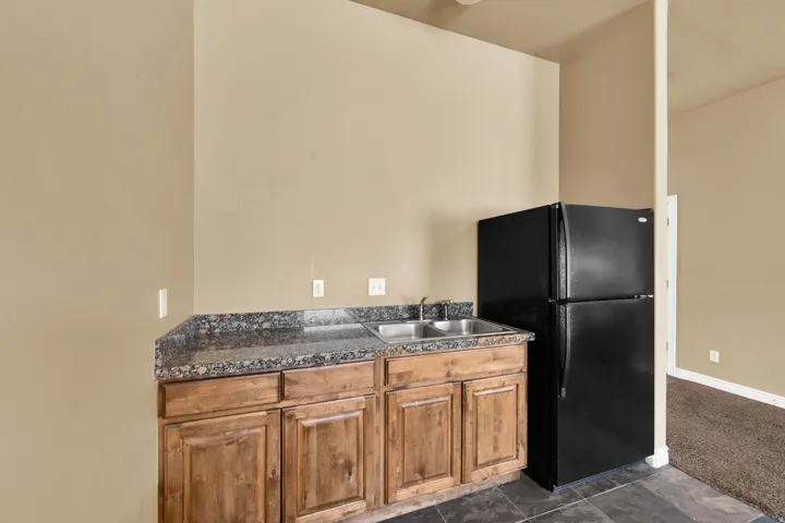 Kitchenette featuring a black refrigerator, dual stainless steel sinks, wood-finish cabinetry, and a speckled countertop
