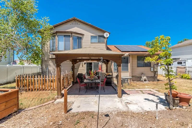 Rear exterior featuring a covered patio with brick pavers, solar panels on the roof, and a bay window on the upper level