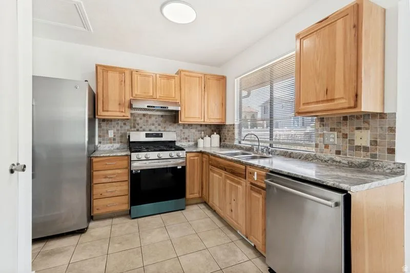 Kitchen featuring wood cabinetry, stainless steel appliances, a mosaic tile backsplash, and light-toned countertops