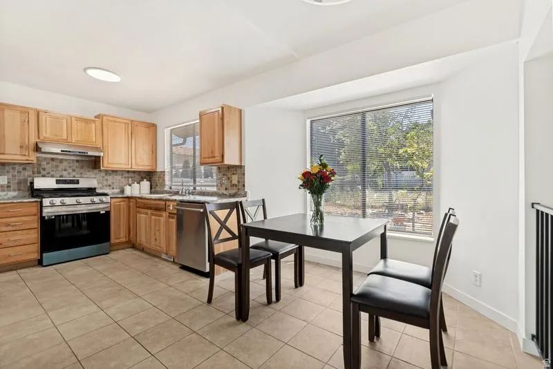 Kitchen featuring light wood cabinetry, stainless steel appliances, tile backsplash, and a ceramic tile floor