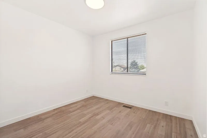 Bright room featuring wood-finish flooring, white walls, and a prominent window with blinds