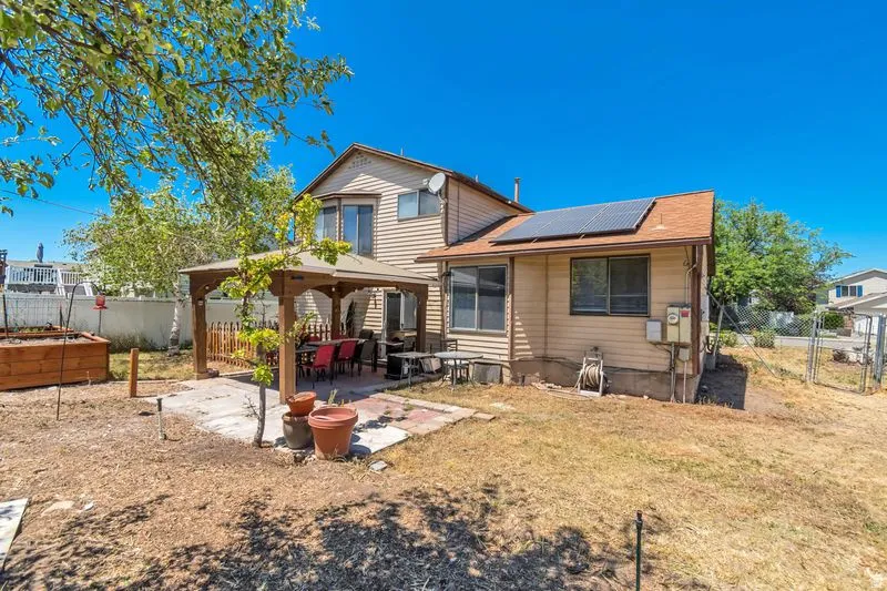Rear exterior featuring a patio with a built-in pergola, bay window, upper-level window, and solar panels on the roof