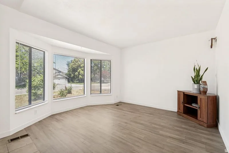 Spacious room featuring a curved bay window with multiple panes, wood-finish flooring, white baseboards, and neutral wall finishes