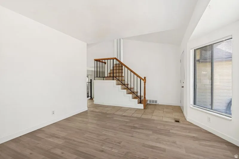 Interior featuring wood-finish flooring, a staircase with wood railing and black spindles, and a tiled entry