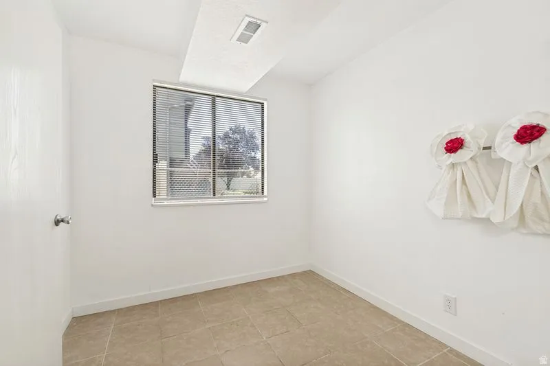 Room featuring tile flooring, white baseboards, a window with horizontal blinds, and white walls