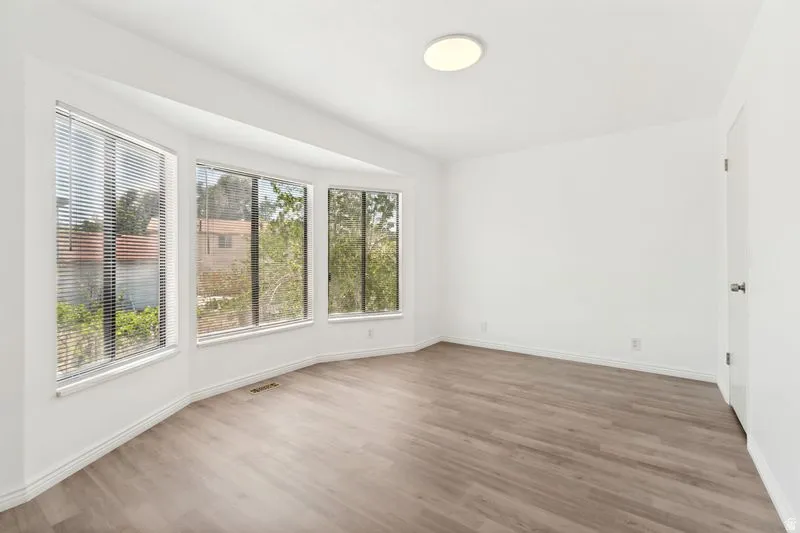 Bay window with multiple large windows, wood-finish flooring, white walls, white trim, and a flush-mount ceiling light fixture