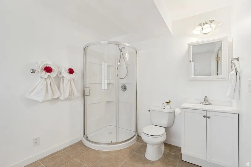 Bathroom featuring a curved glass shower enclosure, white vanity with integrated sink, wall-mounted mirror, and tile flooring