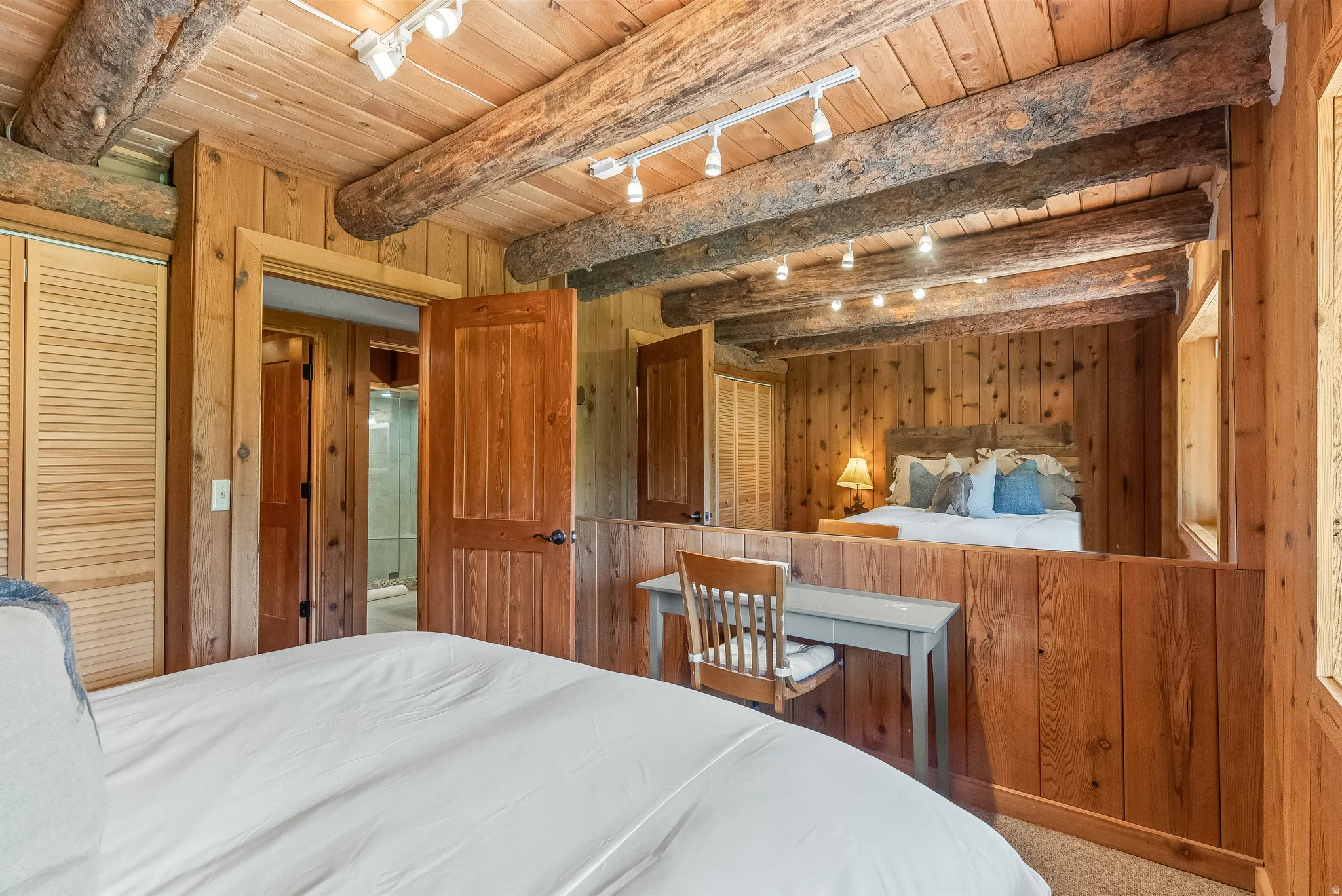 Wood-paneled interior featuring exposed timber beams, track lighting, louvered closet doors, and wood-finish doors