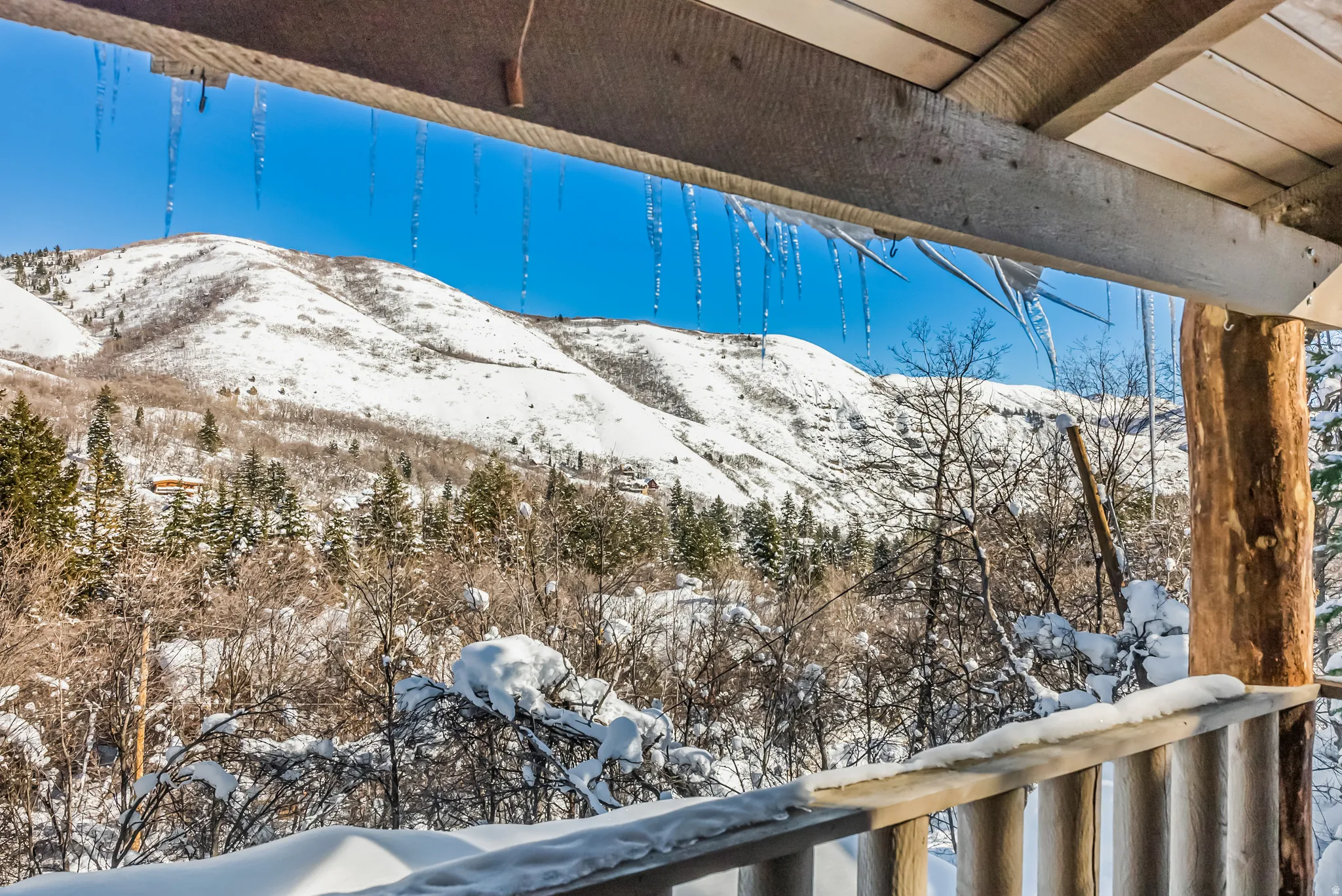 Mountainous landscape featuring snow-covered peaks, evergreen trees, and a wooden balcony railing