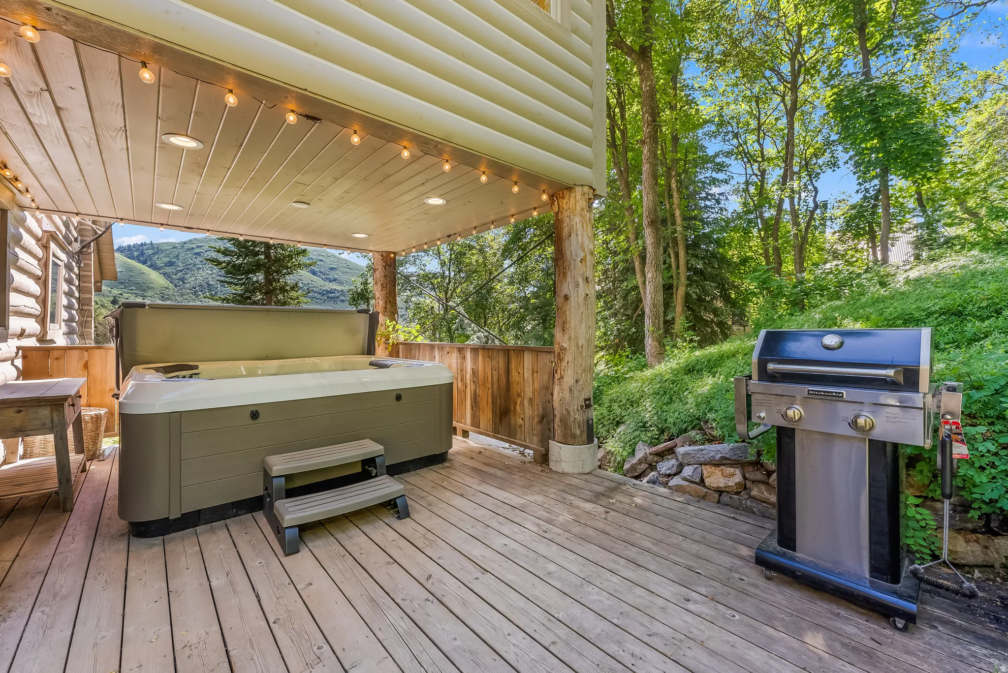 Expansive wood-finish deck featuring a built-in spa, overhead string lighting, recessed ceiling lights, and wooden railings