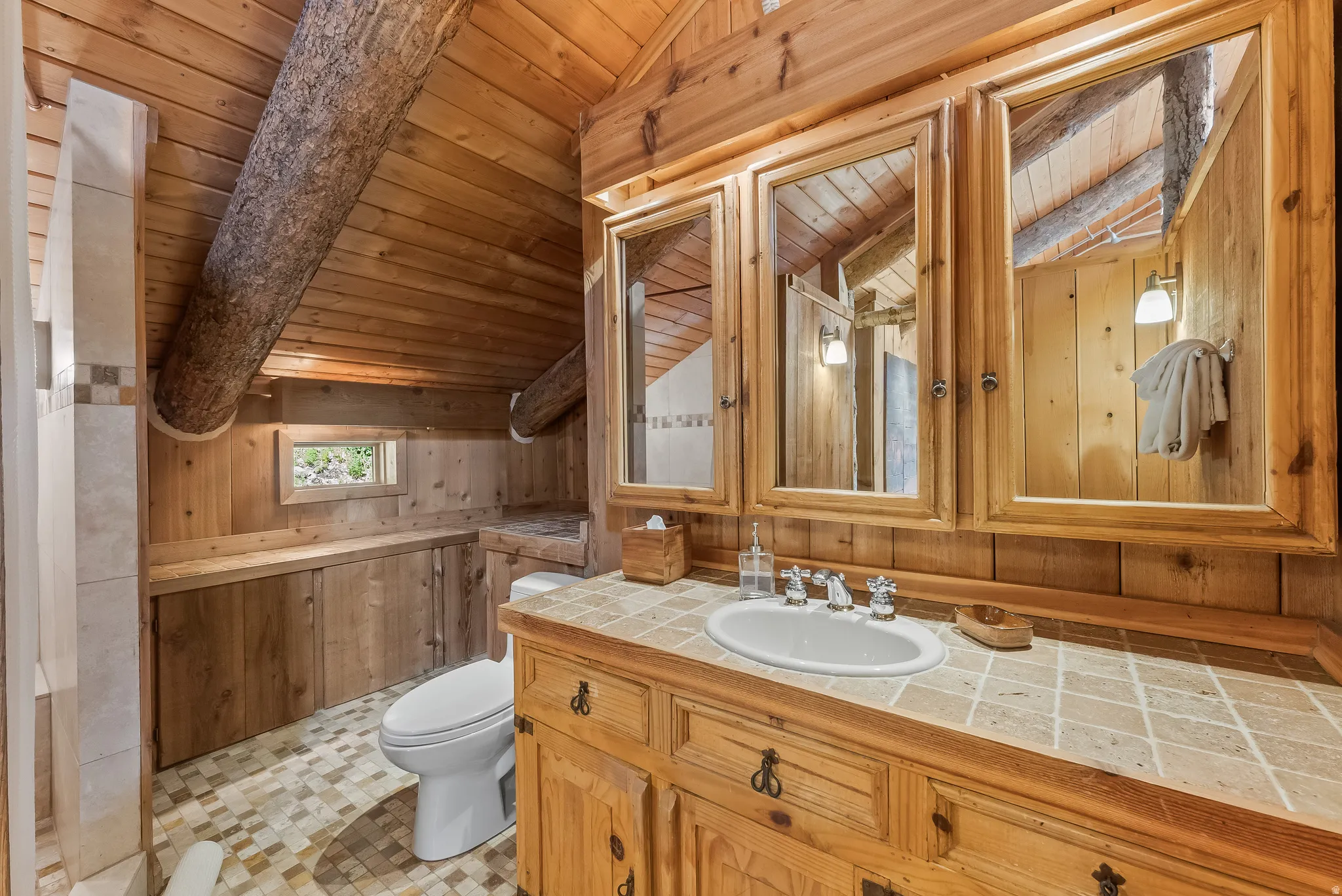 Wood-paneled bathroom featuring a natural wood vanity with a tile countertop and integrated sink