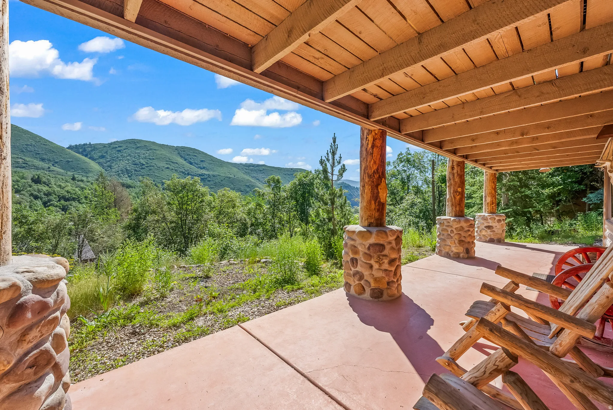 Covered patio featuring a concrete floor, stone pillar bases, and natural wood beams