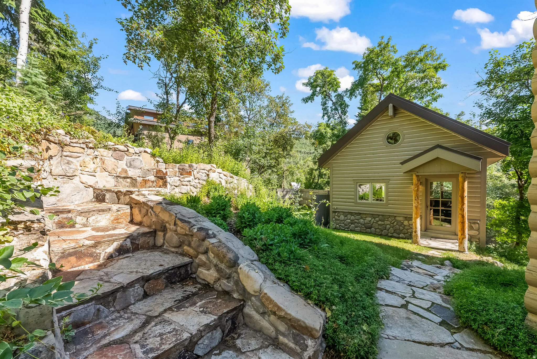 Stone pathway leading to a detached structure with siding and a stone foundation